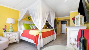 A bedroom with a bed, bedside table, lamp, and a bottle of wine on a table. - Caribbean Paradise-Romantic Oceanfront Canopy King Suite with Breathtaking Views (Myrtle Beach)