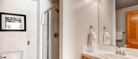 A bathroom with a glass shower enclosure, a white toilet, a wooden vanity with a sink, and a large mirror.