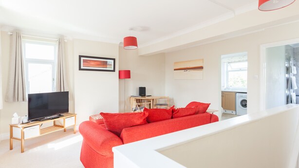 A modern living room with a red sofa, a flat-screen TV, a wooden coffee table, and a small desk with a computer. - Toothbrush Apartments - East Ipswich - Cauldwell Ave (Ipswich)