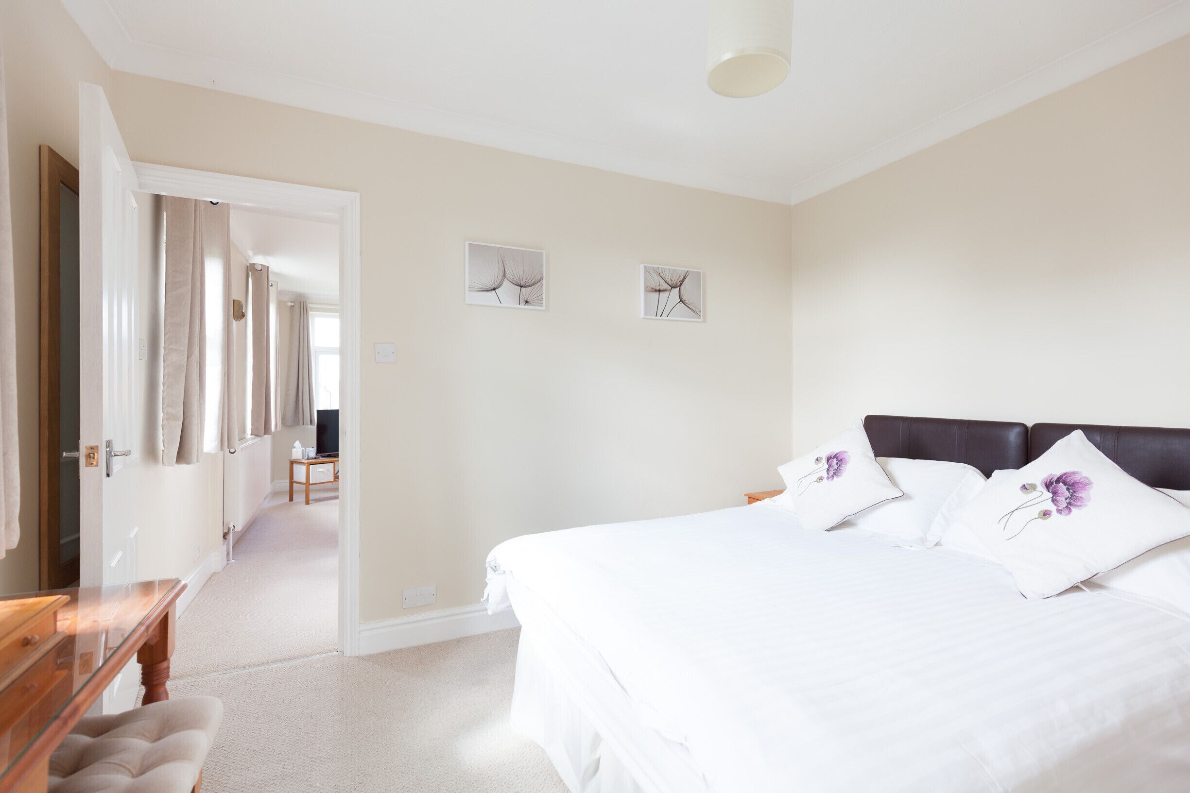 A bedroom with a large bed, a wooden nightstand, and a chair. There is a door leading to another room.