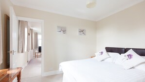 A bedroom with a large bed, a wooden nightstand, and a chair. There is a door leading to another room. - Toothbrush Apartments - East Ipswich - Cauldwell Ave (Ipswich)