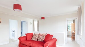 A spacious living room with a red sofa, a red pendant light, and a view of a kitchen and bathroom through an open door. - Toothbrush Apartments - East Ipswich - Cauldwell Ave (Ipswich)