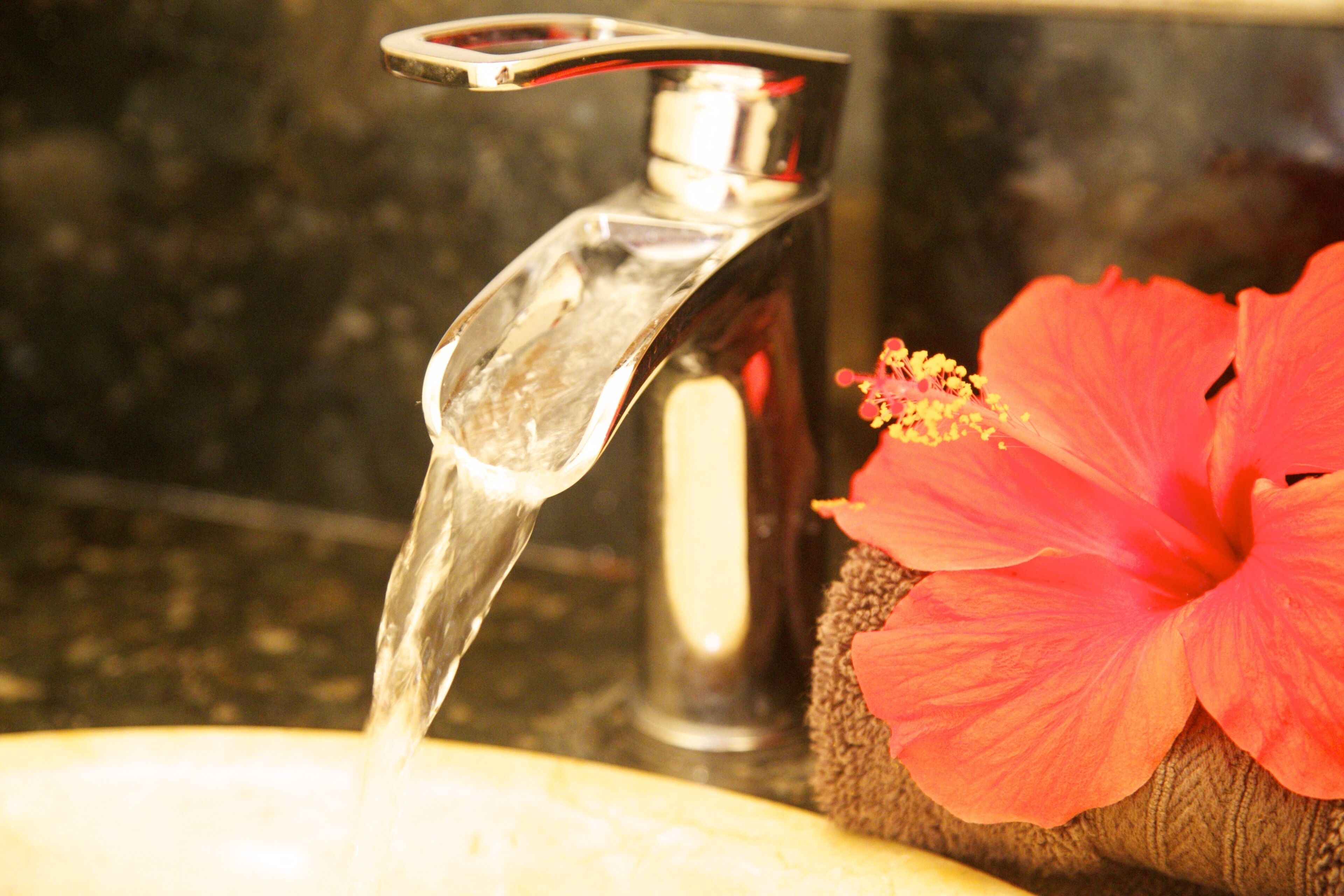 A bathroom sink with a running faucet and a hibiscus flower beside it.