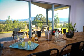 A dining table with a view of the outdoors, a pitcher of water, a bottle of Corona beer, and a potted plant. - Pindara - Modern, 5 bedroom house with fabulous valley views! (Broke)