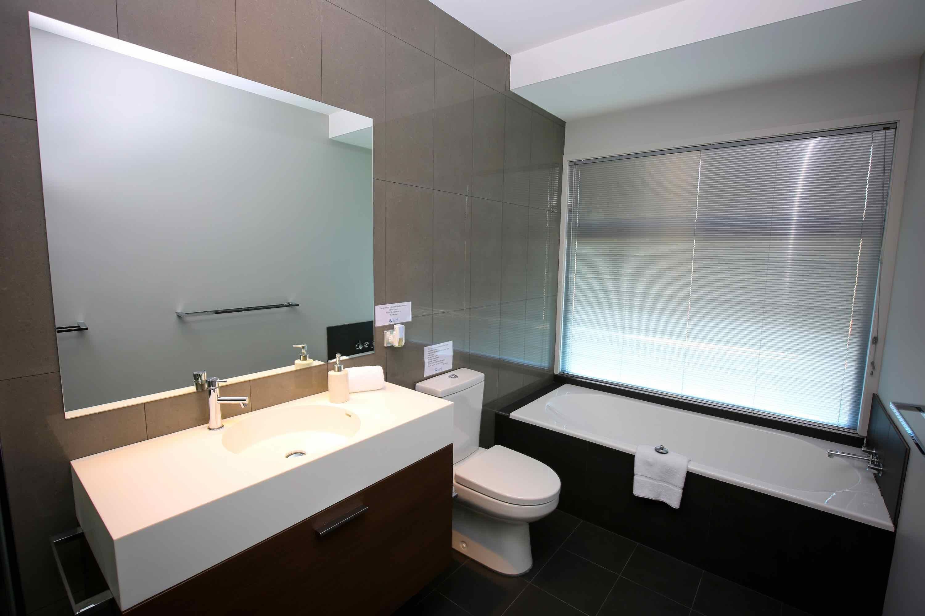 A modern bathroom with a large mirror, a sink, a toilet, and a bathtub.