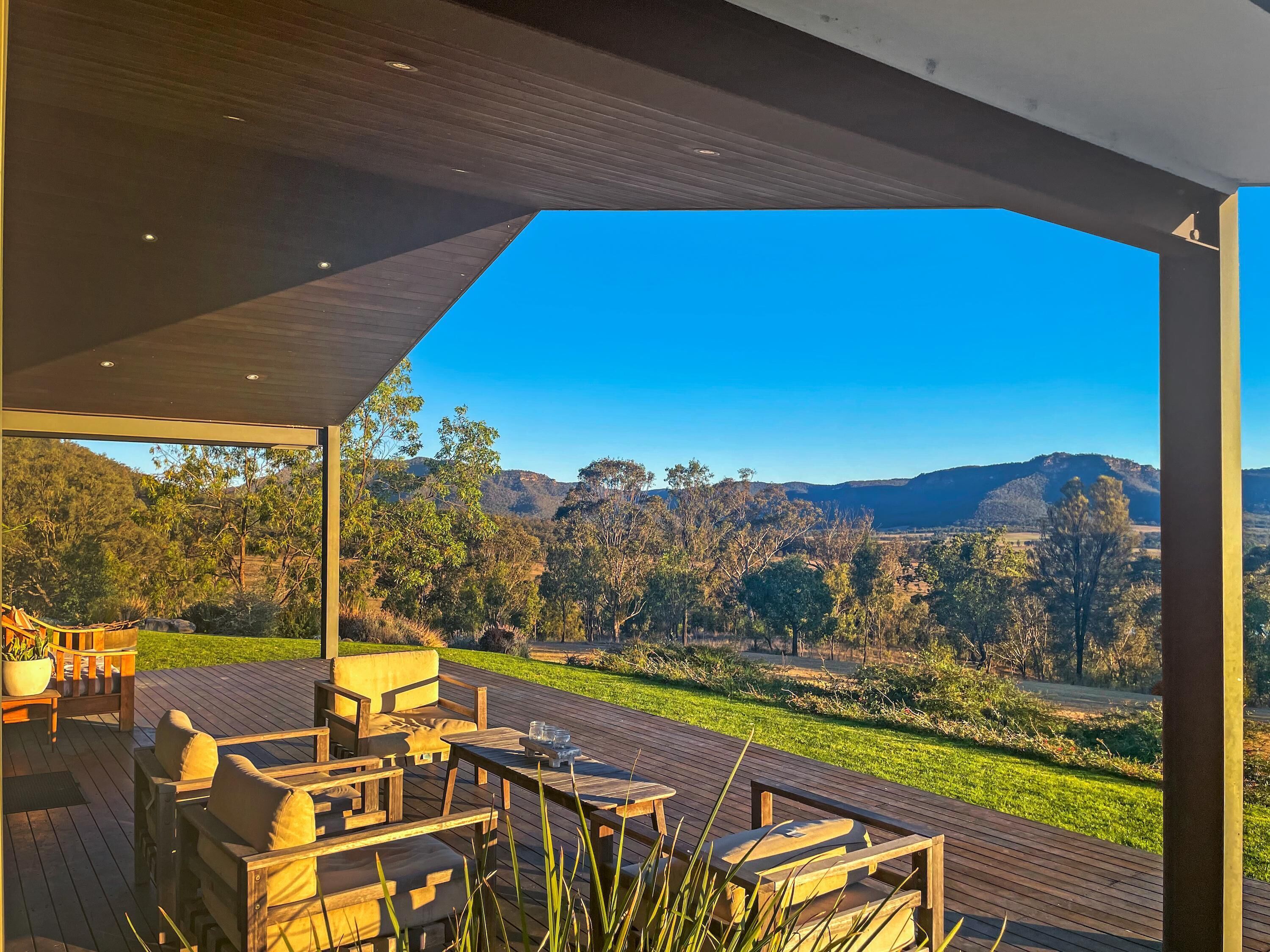 A covered outdoor seating area with wooden furniture and a view of a hilly landscape.