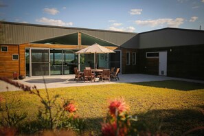 A modern house with a large glass door, a patio with a table and chairs, and a grassy yard. - Pindara - Modern, 5 bedroom house with fabulous valley views! (Broke)