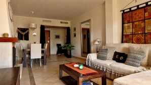 Una sala de estar con sofá, mesa de centro, mesa de comedor con sillas y una puerta que da a otra habitación.