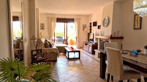 Amplia sala de estar con sofá, mesa de centro y mesa de comedor. Se observa un televisor, chimenea y candelabro.