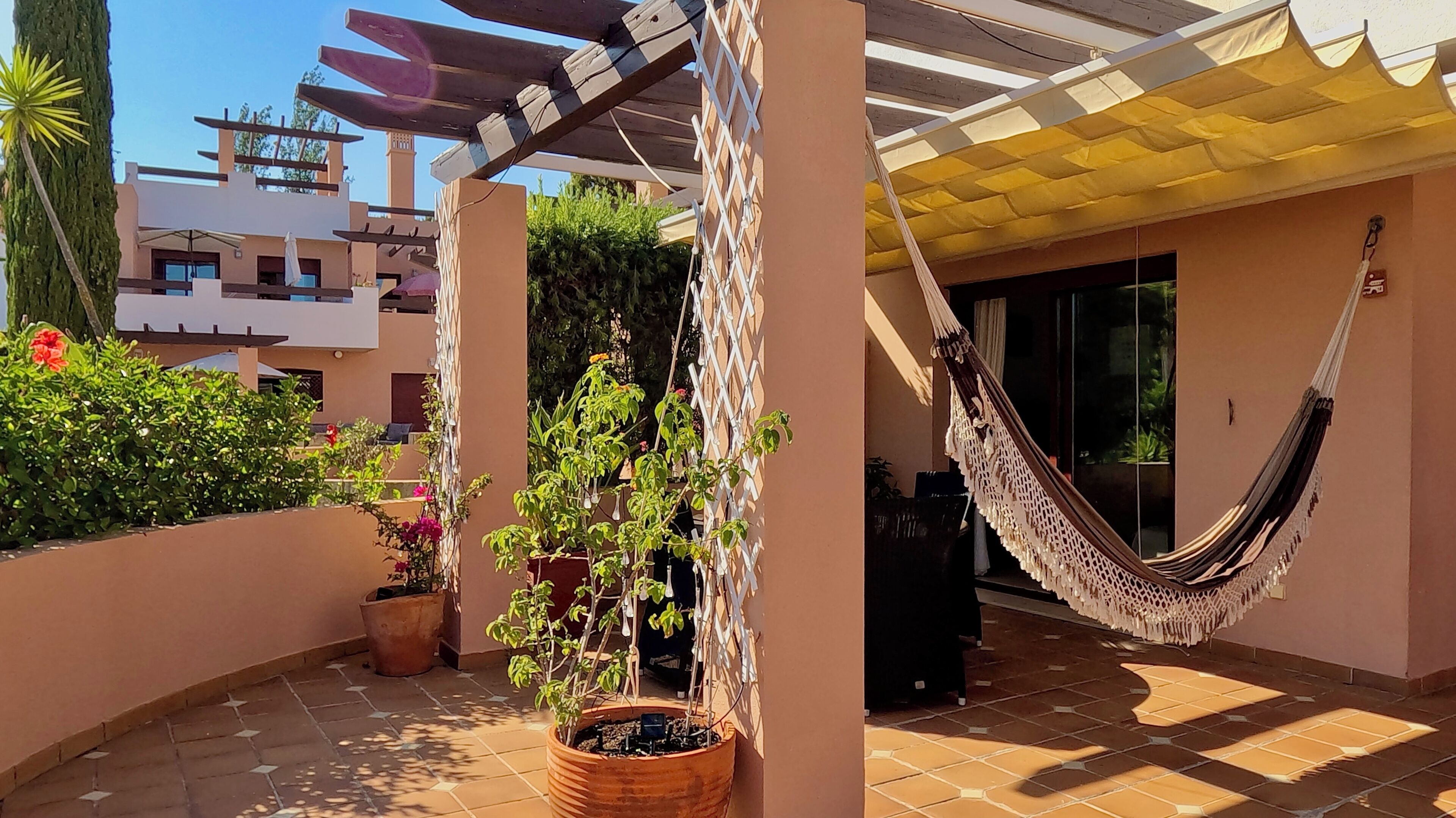 En uteplats med en hängmatta, krukväxter och en pergola.