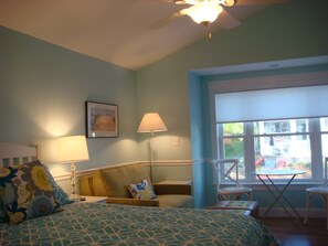 Un dormitorio con una cama, una silla, una mesa, una lámpara y una ventana que da a vistas del exterior.