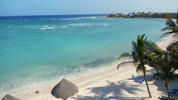 A beach with clear turquoise water, white sand, and palm trees. There are lounge chairs and a thatched umbrella on the beach. - Beautiful & Cozy Space in Half Moon Bay Akumal (Akumal)