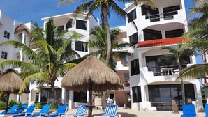 A beachfront hotel with multiple balconies, palm trees, and sun loungers. - Beautiful & Cozy Space in Half Moon Bay Akumal (Akumal)