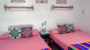 A room with two beds, each with colorful striped bedspreads and patterned pillows. There is a small wooden nightstand with a lamp and a few items on it. - Beautiful & Cozy Space in Half Moon Bay Akumal (Akumal)