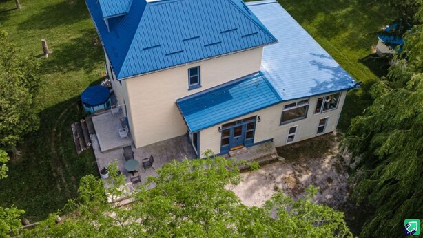 Une maison à deux étages, avec un toit bleu, entourée d’une végétation luxuriante.