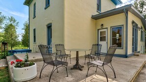 Une terrasse avec une table ronde et quatre chaises, entourée d’un sol en béton, avec une maison en arrière-plan.