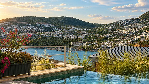 A pool with a view of a hillside town, a bench, and some plants.