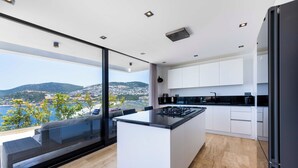A modern kitchen with a large island, white cabinets, and a view of the sea and hills.