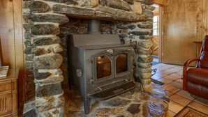 A stone fireplace with a wood-burning stove, a leather chair, and a wooden cabinet. - (69) Bordentown West at The Redwoods In Yosemite (Yosemite National Park)