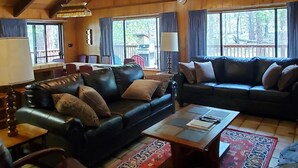 A spacious living room with a high ceiling, wooden beams, leather sofas, a coffee table, and a large window offering a view of the outdoors. - (69) Bordentown West at The Redwoods In Yosemite (Yosemite National Park)