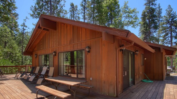 A wooden cabin with a deck, lounge chairs, and a picnic table. - (69) Bordentown West at The Redwoods In Yosemite (Yosemite National Park)