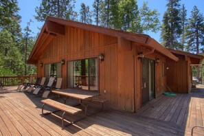 A wooden cabin with a deck, lounge chairs, and a picnic table.