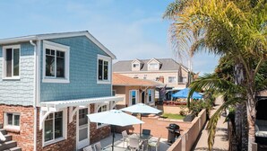 A two-story house with a patio area featuring a table and chairs, a barbecue grill, and a covered seating area with umbrellas.