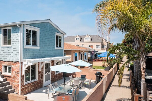 Une maison à deux étages dotée d’un patio comprenant une table et des chaises, un barbecue et un espace salon couvert.