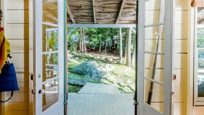 Une porte en bois ouverte donne sur un espace extérieur abrité, doté d’un plancher en bois et d’un banc.