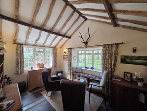 A rustic room with exposed wooden beams, a fireplace, a dining table, and a window with curtains.