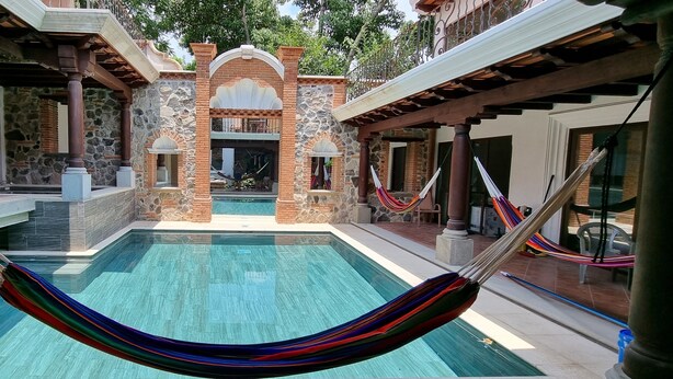 A pool area with a hammock, stone walls, and a view of the interior. - Apartamentos los Nazarenos PRIVATE APT 4 - heated swimming pool, jacuzzi and gym (Antigua Guatemala)