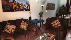 A living room with two brown leather sofas, a coffee table with a colorful woven placemat, and a painting of a landscape on the wall. - Apartamentos los Nazarenos PRIVATE APT 4 - heated swimming pool, jacuzzi and gym (Antigua Guatemala)