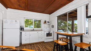 Une cuisine avec des meubles blancs, un plafond en bois, une fenêtre et un coin bar avec des tabourets.
