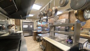 A commercial kitchen with stainless steel appliances, hanging pots, and a food service display. - Beautiful Lodge and Private 600 acre Canyon Paradise (Altamont)