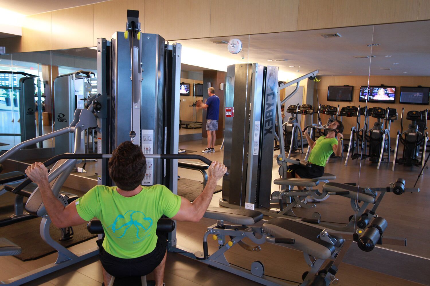 Ein Fitnessstudio mit verschiedenen Trainingsgeräten, darunter ein Kabelzug und Laufbänder.