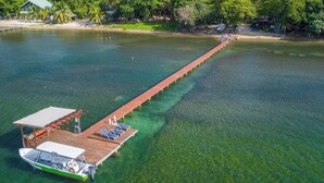 A wooden pier extending into a clear lake, with a boat docked at the end. - Stay & Dive! Ocean front, Cozy Casita steps to the waters edge!  (Roatan, Bay Islands)