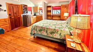 A compact bedroom with a bed, a nightstand, a lamp, a ceiling fan, and a kitchenette area. - Stay & Dive! Ocean front, Cozy Casita steps to the waters edge!  (Roatan, Bay Islands)