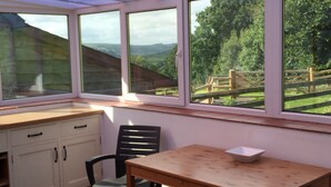 A conservatory with a wooden table and chairs, a white cabinet, and a view of a wooden fence and greenery. - Llwyn Llwyd Cottage Brecon  Group and contractor friendly. Garden. Dog friendly  (Aberyscir)