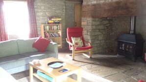 A cozy living room with a stone wall, a fireplace, a bookshelf, a red armchair, and a sofa. - Llwyn Llwyd Cottage Brecon  Group and contractor friendly. Garden. Dog friendly  (Aberyscir)