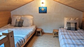 A cozy attic bedroom with two beds, a small stool, and a wall-mounted light fixture. - Light airy Chalet - Mountain And Waterfall Views. Excellent access all Amenities (Samoëns)