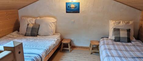 A cozy attic bedroom with two beds, a small stool, and a wall-mounted light fixture.