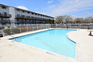 Une piscine rectangulaire entourée d’une clôture blanche, elle-même bordée d’un immeuble doté de nombreux balcons.