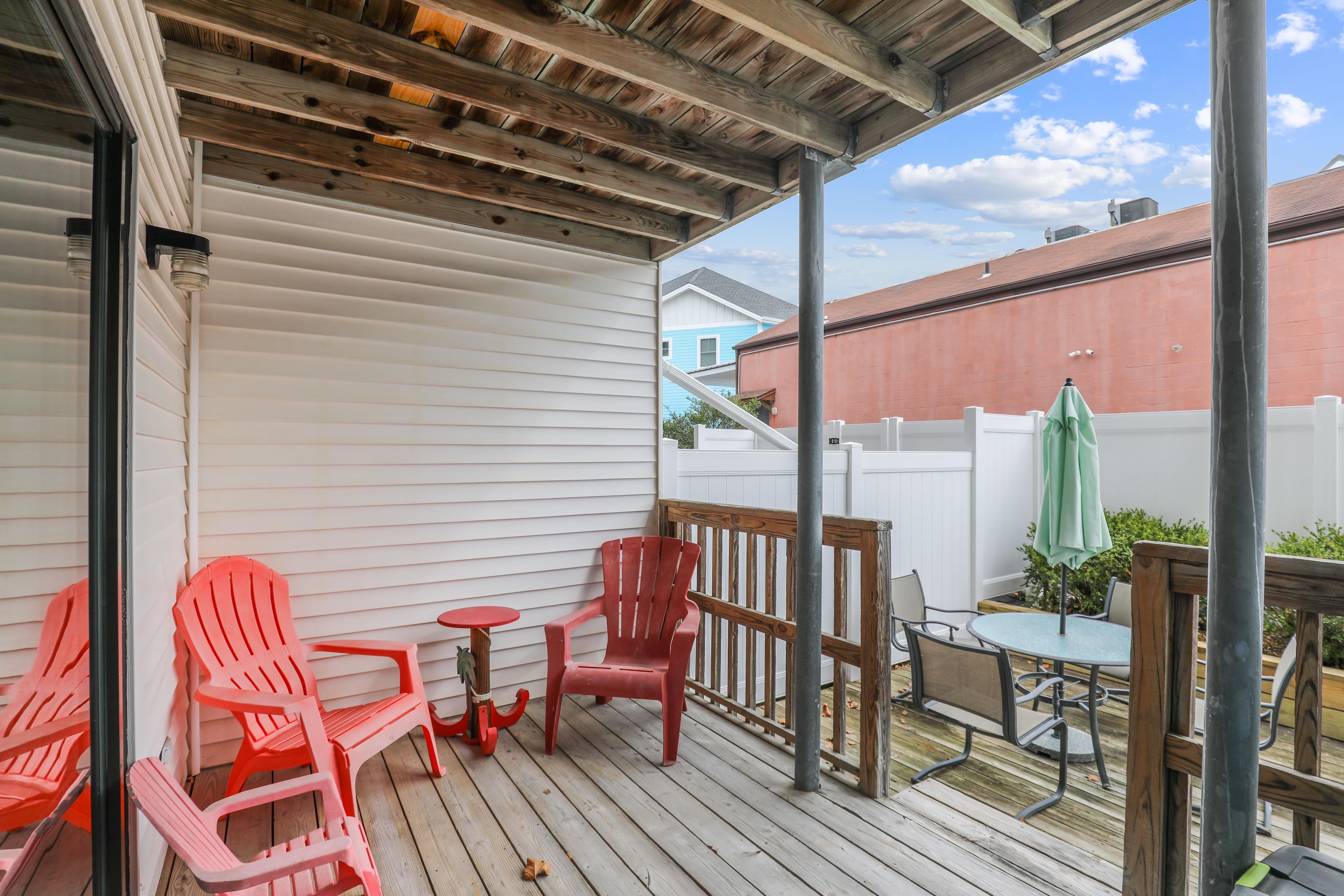 Une terrasse extérieure couverte, avec des chaises rouges et une table, une clôture blanche et un bâtiment en arrière-plan.