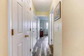 Un couloir avec des portes blanches, un plancher en bois et un tableau accroché au mur.
