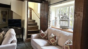 A cozy living room with a sofa, patterned cushions, a television, and a staircase leading to another room.