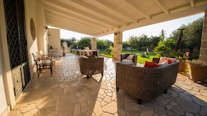 A covered patio with stone flooring, wicker furniture, and a view of a lush garden. - "VILLA ARGENTI" - VILLA WITH POOL BETWEEN SEA AND COUNTRYSIDE IN SALENTO (Melendugno (LECCE))