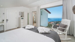 Un dormitorio con una cama grande, una silla blanca y vista al mar.