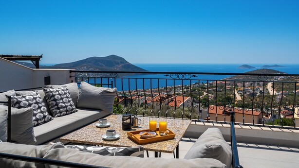 Un balcón con sofá y mesa, con vista a un pueblo costero y una montaña.