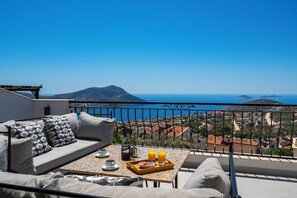 A balcony with a sofa and table, overlooking a coastal town and a mountain. - Luxury Villa With Large Private Pool And Sea Views (Kalkan)