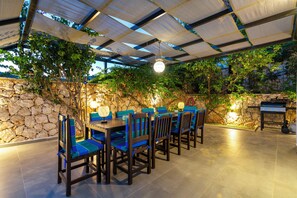 An outdoor patio with a stone wall, wooden tables, and chairs. - Luxury Villa With Large Private Pool And Sea Views (Kalkan)
